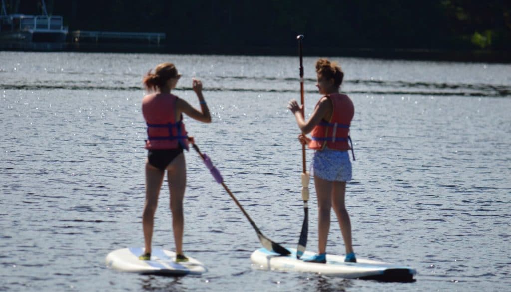 Camper friends standing on paddle boards on Hunter Lake at WeHaKee Camp for Girls.