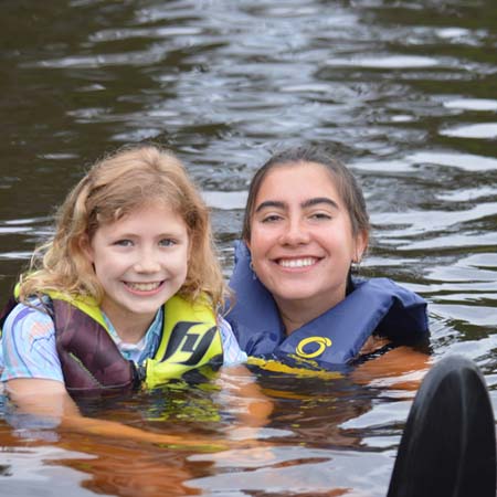 WeHaKee Camp for Girls counselor in the lake with camper teaching her to waterski.