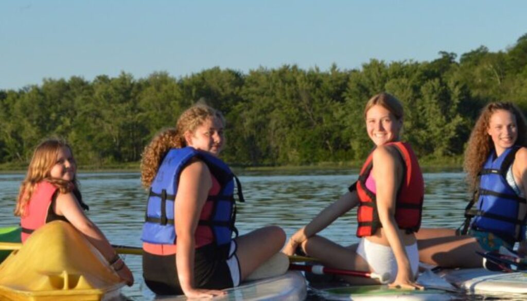 WeHaKee Camp for Girls campers posing on their kayaks and paddleboards, smiling during a fun summer day on Hunter Lake.