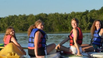 WeHaKee Camp for Girls campers posing on their kayaks and paddleboards, smiling during a fun summer day on Hunter Lake.