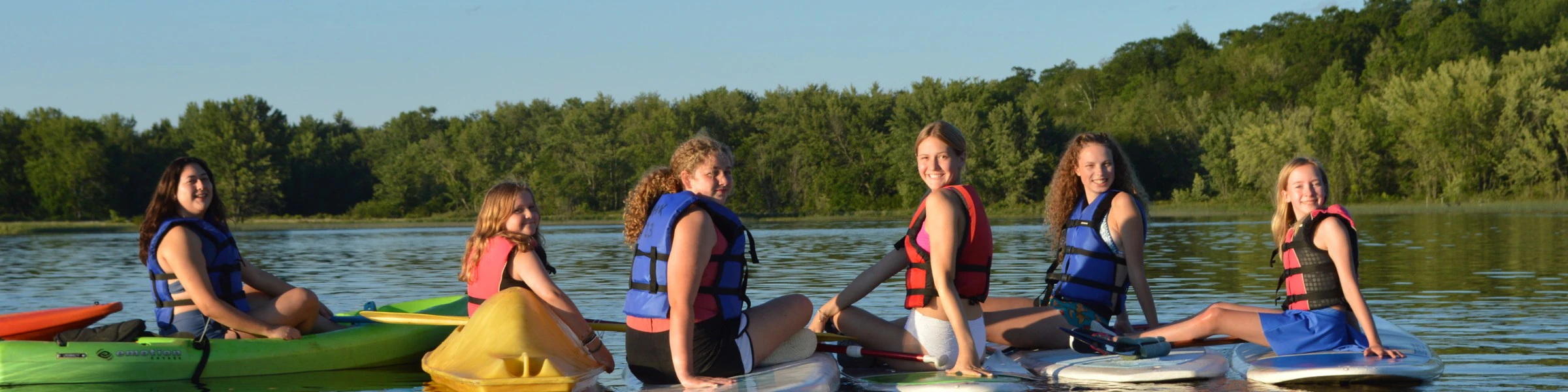 WeHaKee Camp for Girls campers posing on their kayaks and paddleboards, smiling during a fun summer day on Hunter Lake.